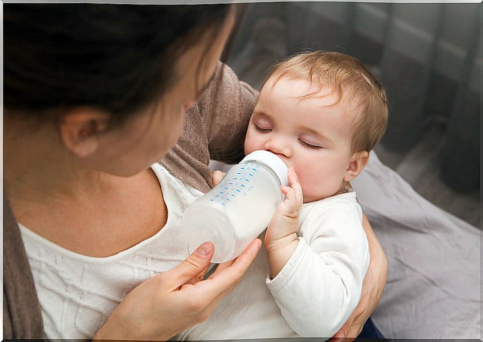 Baby taking the bottle in a sitting position to avoid colic in children.